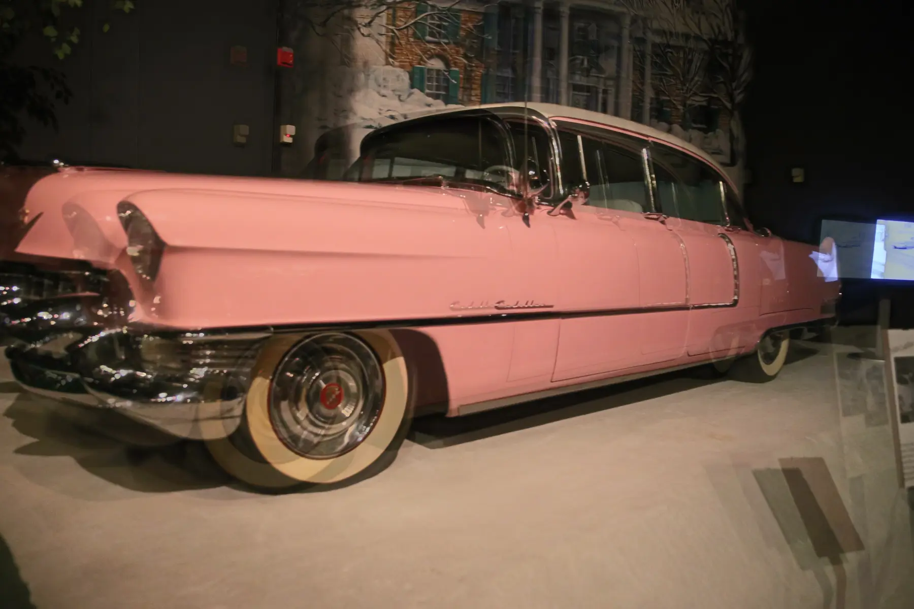 Elvis Presley’s actual pink-and-white 1955 Cadillac Series 60 Fleetwood Special displayed behind glass at the Graceland automobile museum.
