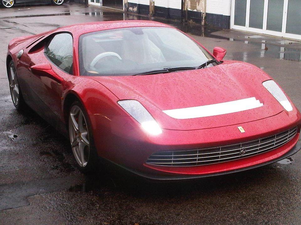 Front-left view of Eric Clapton’s actual red Ferrari SP12 EC one-off on wet pavement, with no registration visible.