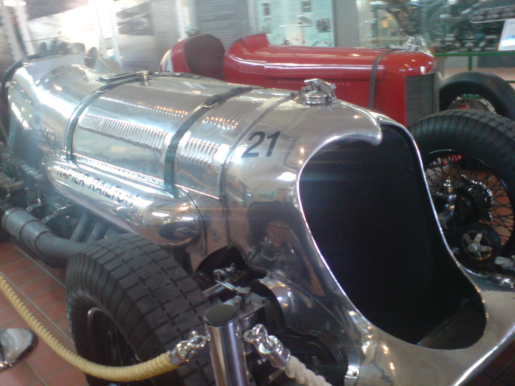 The actual surviving silver Napier-Railton race car displayed at Brooklands Museum with black number 21 on its streamlined body.