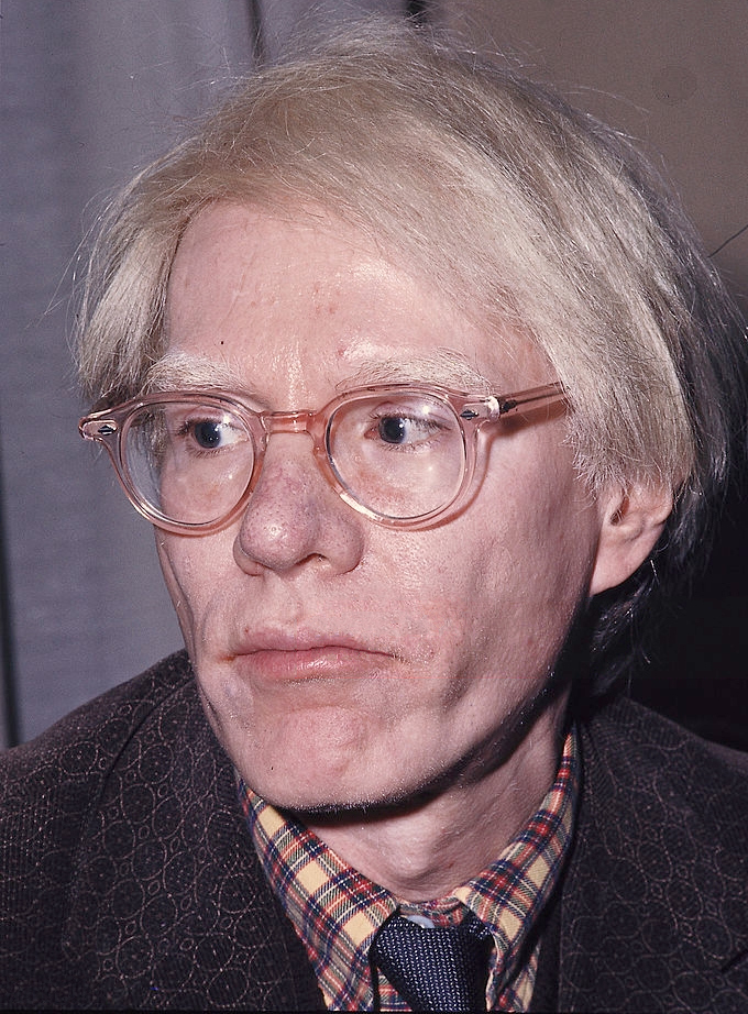 Andy Warhol wearing clear-framed glasses in a 1975 identification portrait.