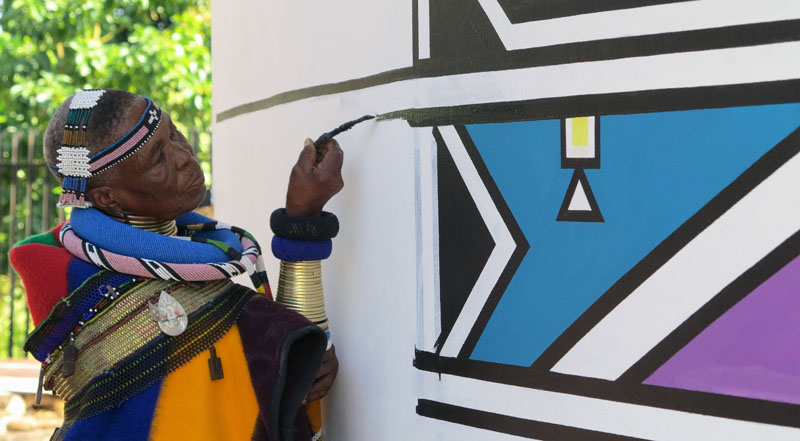 Esther Mahlangu painting a geometric wall design with a chicken-feather brush at her home in 2015, photographed by Freddejager.