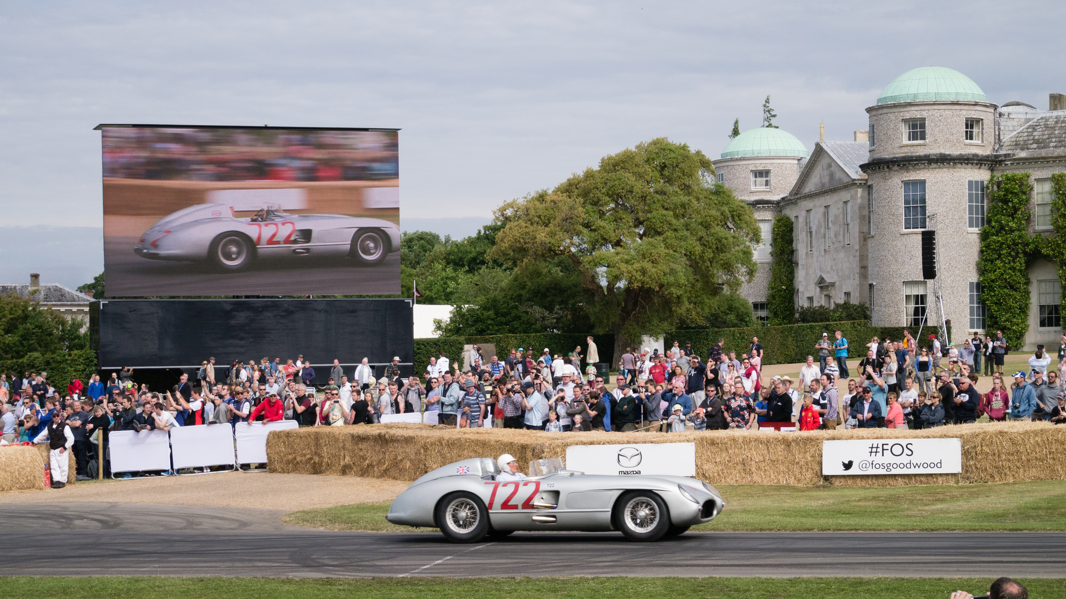 Stirling Moss driving the silver Mercedes-Benz 300 SLR number 722 past spectators at Goodwood in 2015.